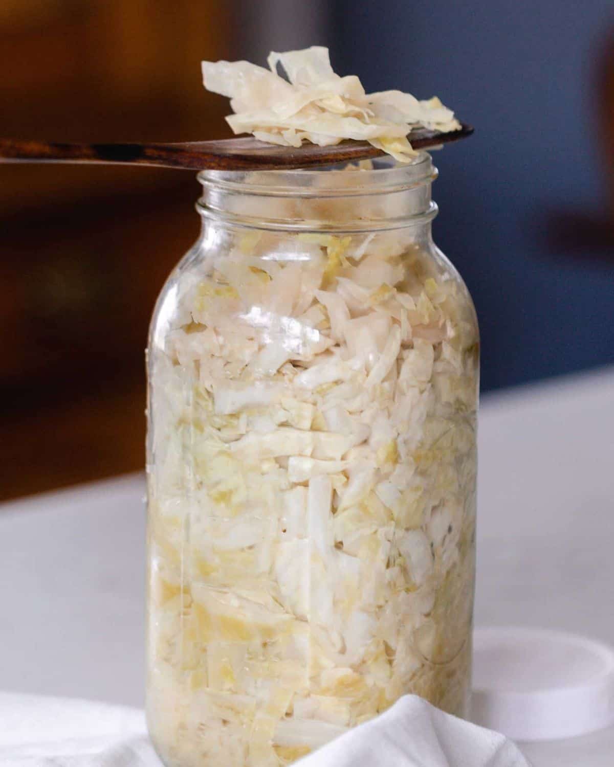 A wooden spoon scooping out sauerkraut from a large mason jar.