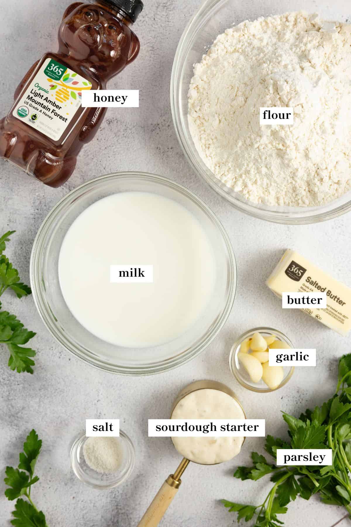 Bowls o flour, sourdough starter, milk, and measuring cup of other ingredients on a countertop.