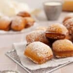 sourdough beignets stacked on a wire rack with powdered sugar.