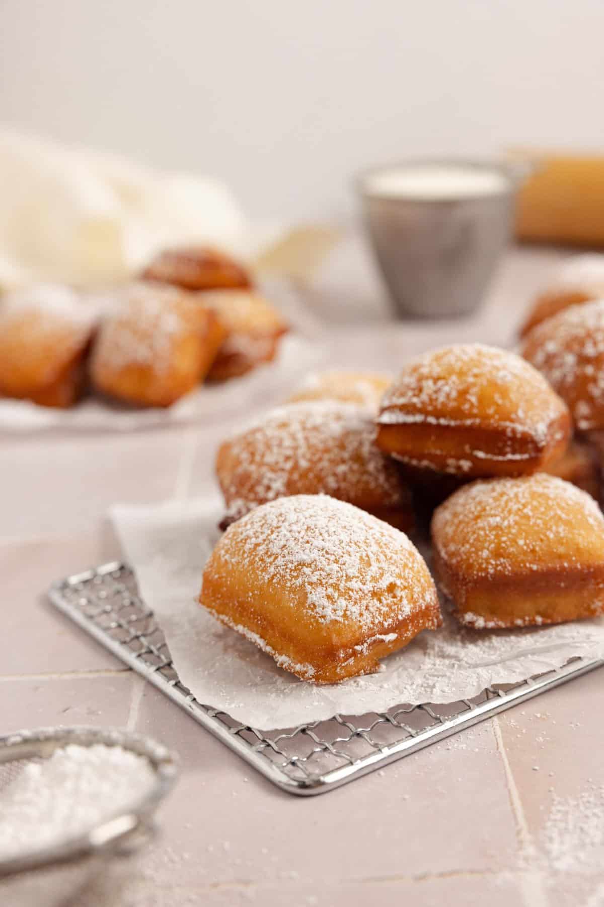 sourdough beignets stacked on a wire rack with powdered sugar.