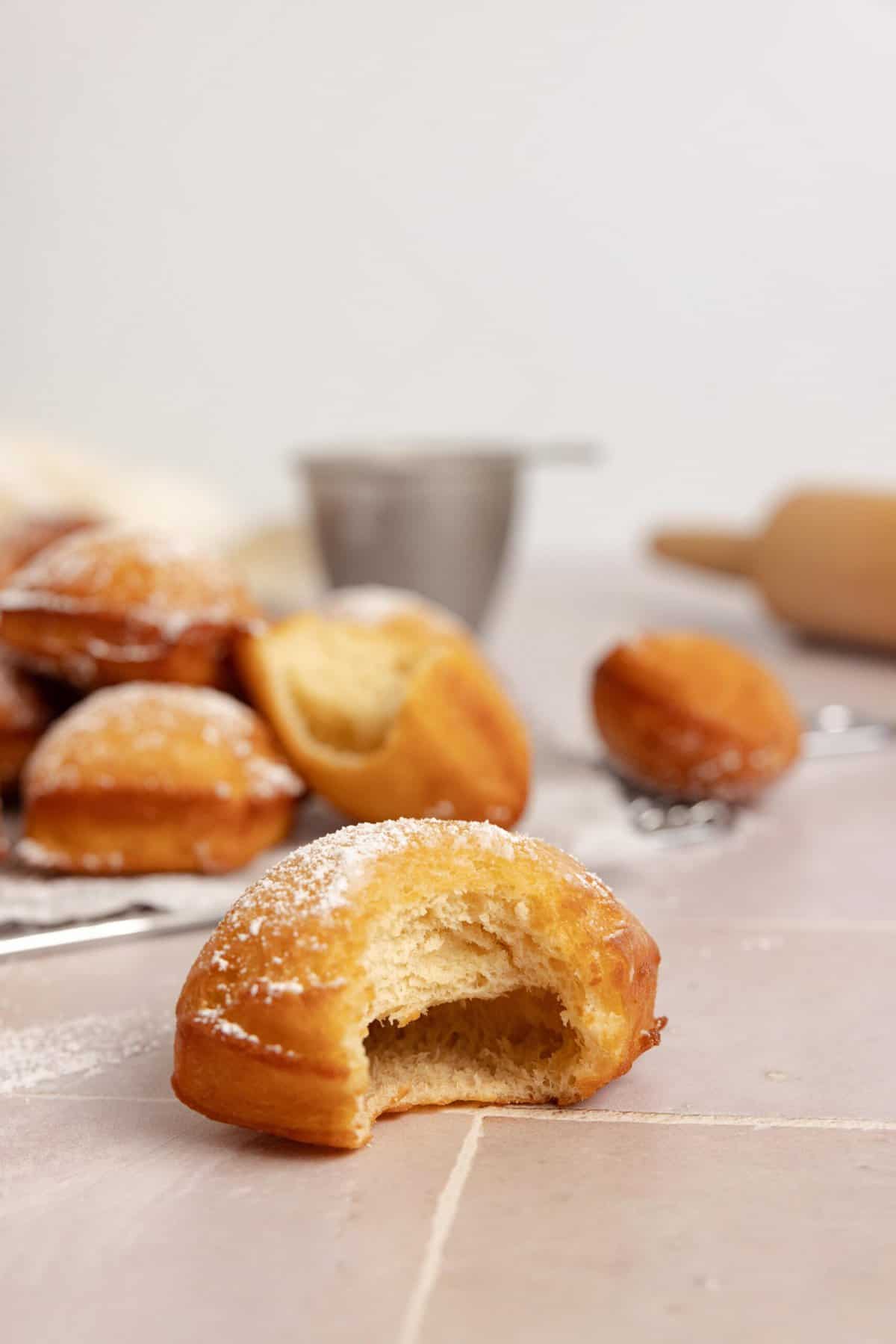 Sourdough beignet with a bite taken out on a countertop with more beignets in the background.