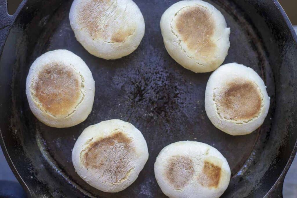 Sourdough discard English muffins cooking on a cast iron skillet.