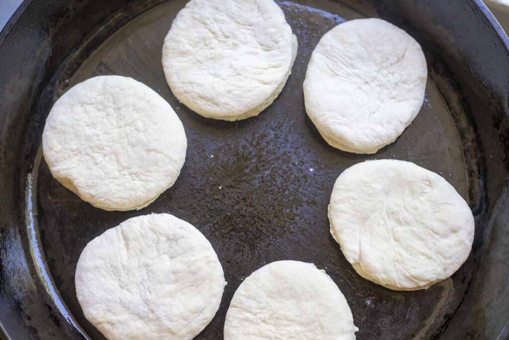 English muffin dough cooking in a cast iron skillet.