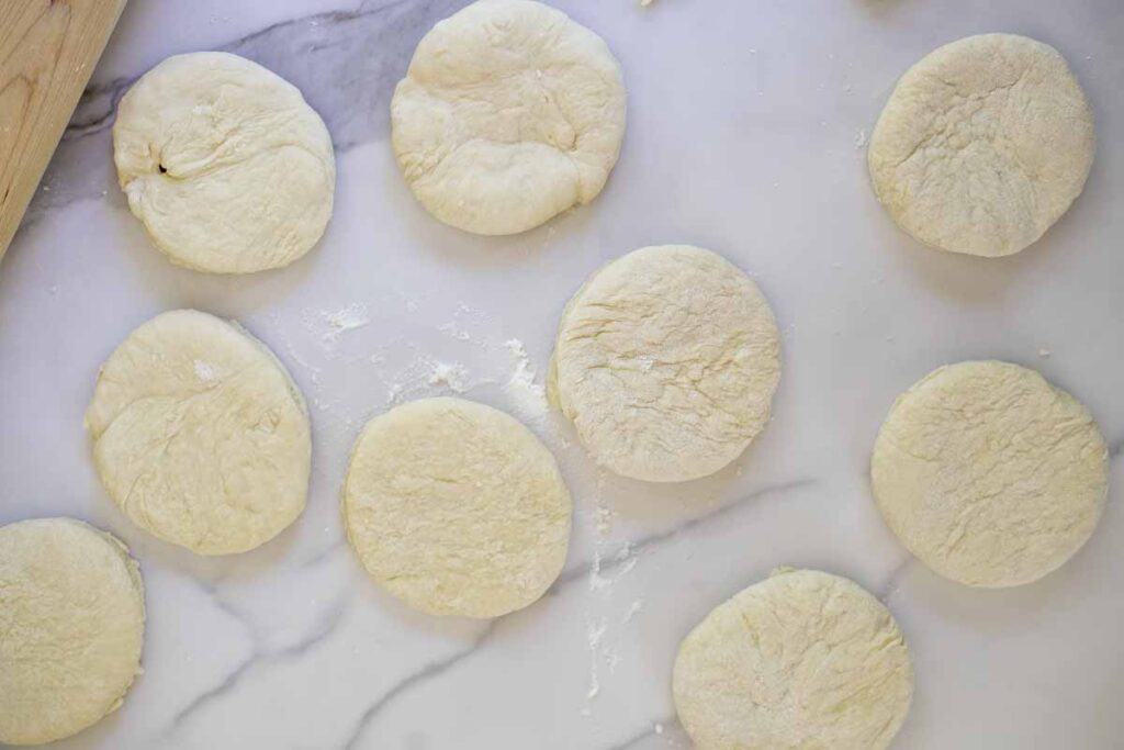 English muffin dough cut up on a marble countertop.