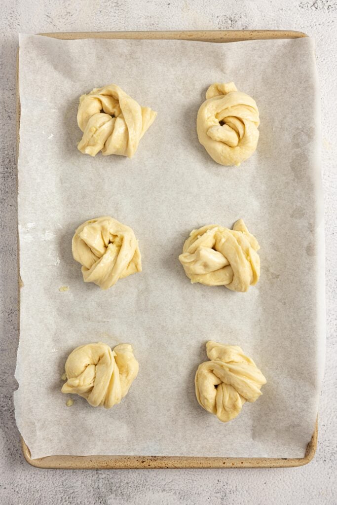 Garlic knot dough twisted together on parchment lined baking sheet.