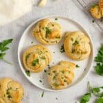 A plate with four sourdough garlic knots topped with parsley. The plate is surrounded with more knots, fresh parsley, garlic, and flour.