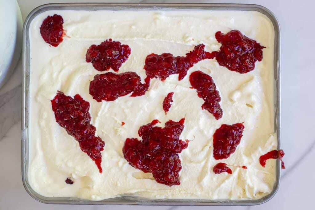 Cheese cake ice cream with blobs of strawberry jam on top in a metal dish.