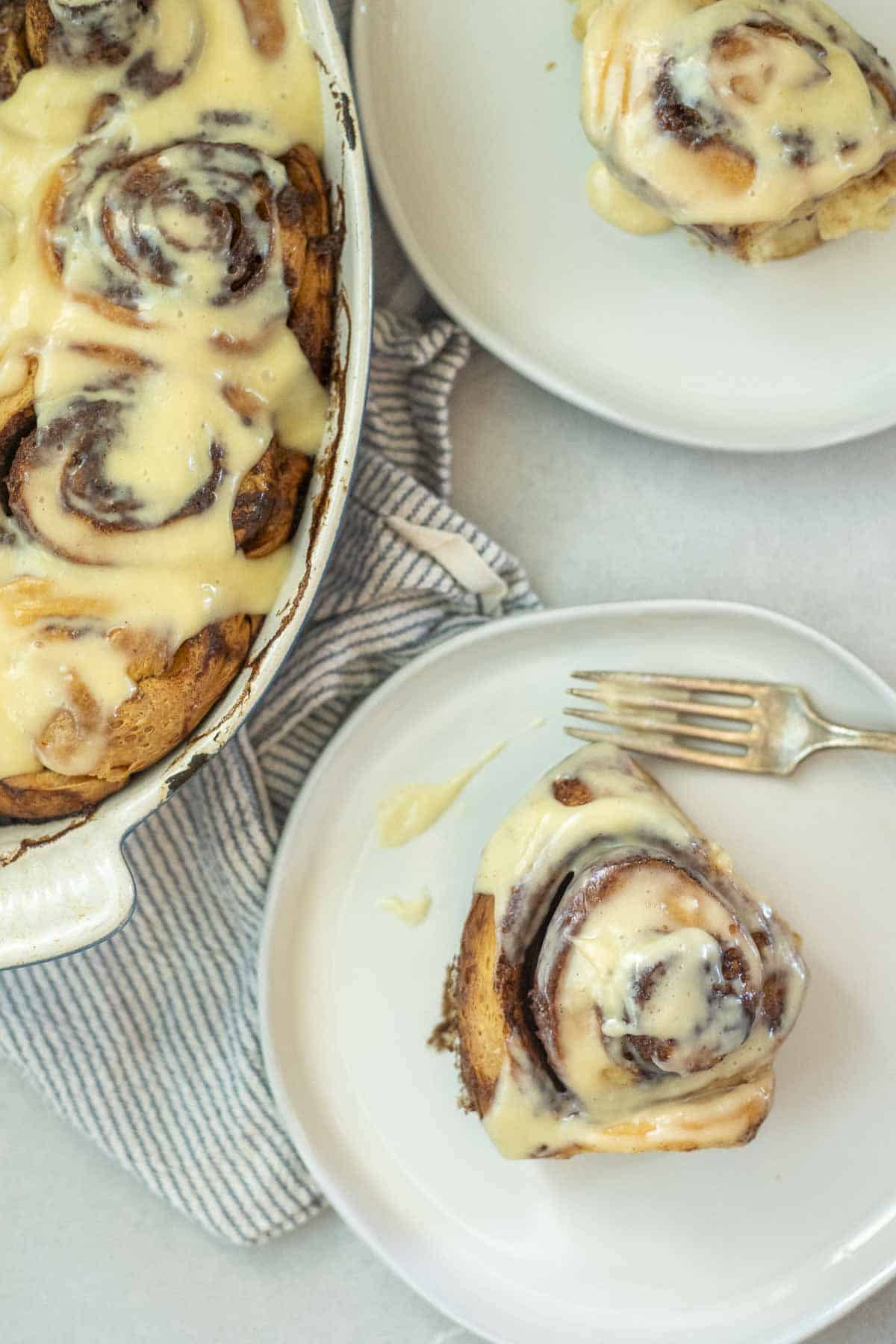 a cinnamon roll on a plate with more rolls in a backing pan in the background.