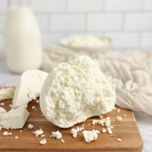 Farmers cheese on a cutting board with a glass of milk in the background.