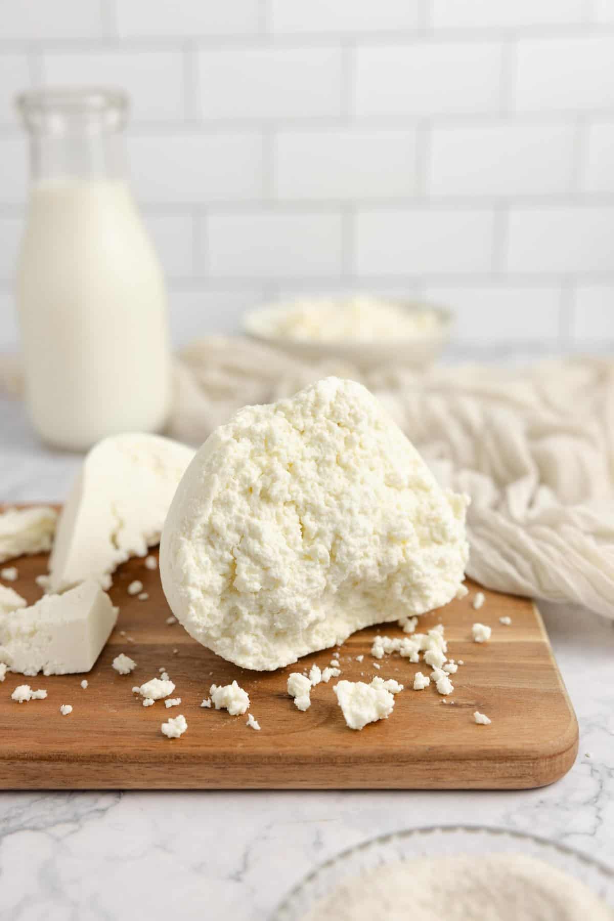 Farmers cheese on a cutting board with a glass of milk in the background.