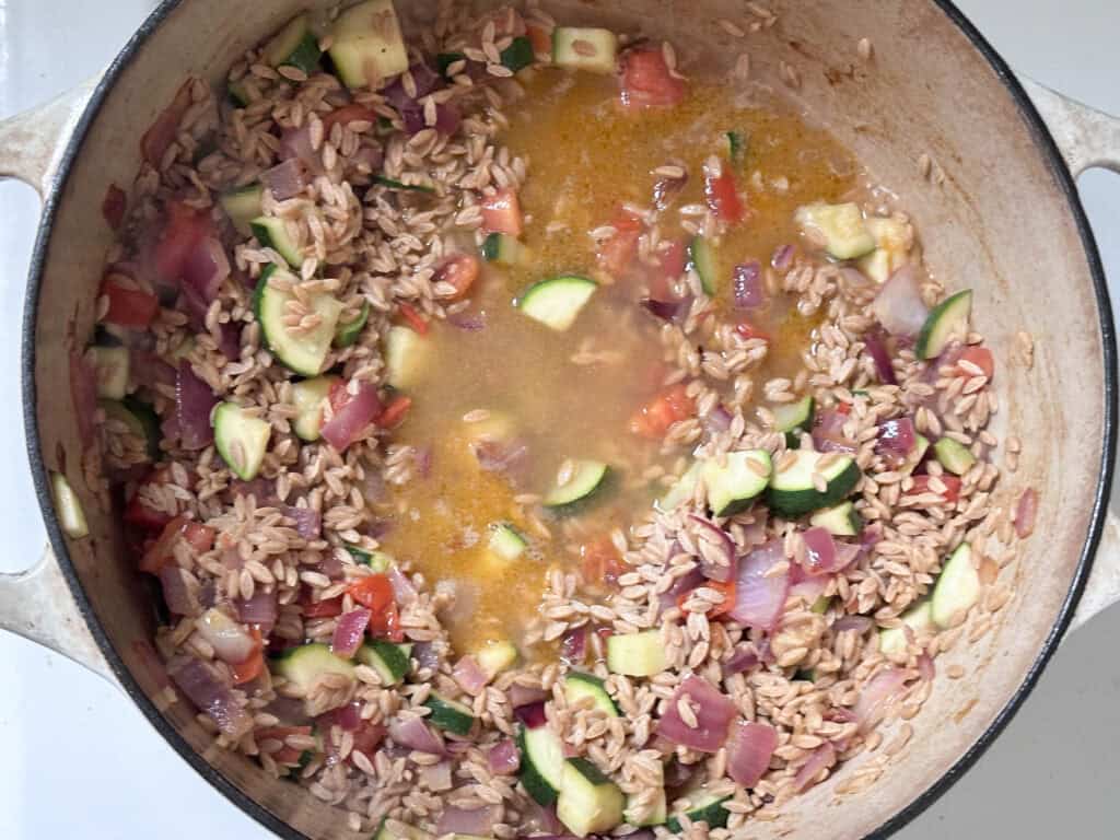 Vegetables cooking with orzo pasta and bone broth. 