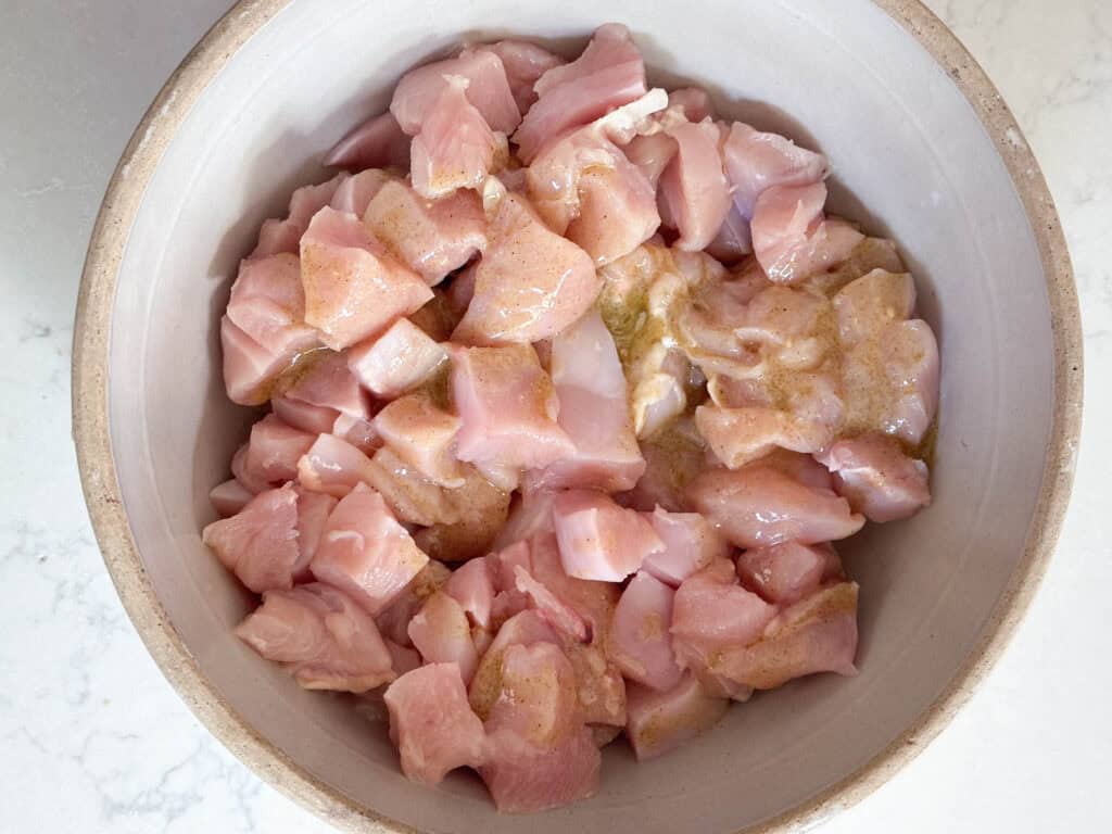 Chicken diced into cubes covered in marinade in a small bowl. 