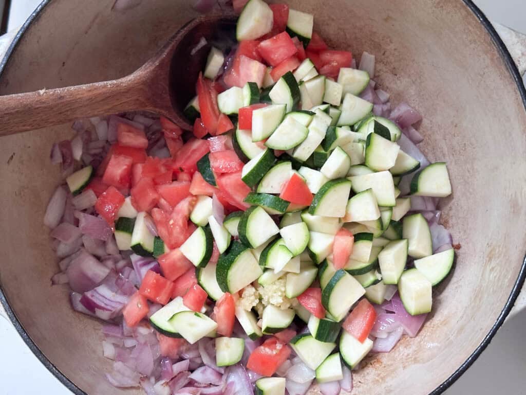 Zucchini, onions, and tomato cooking in a Dutch oven.