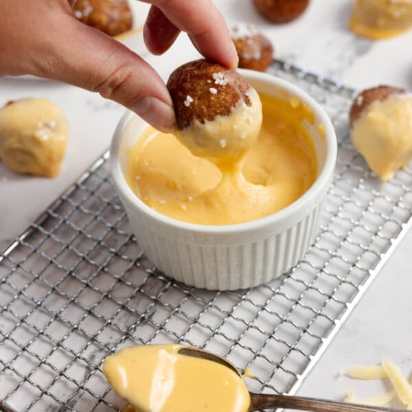 hand dipping pretzel into cheese sauce on a wire rack.