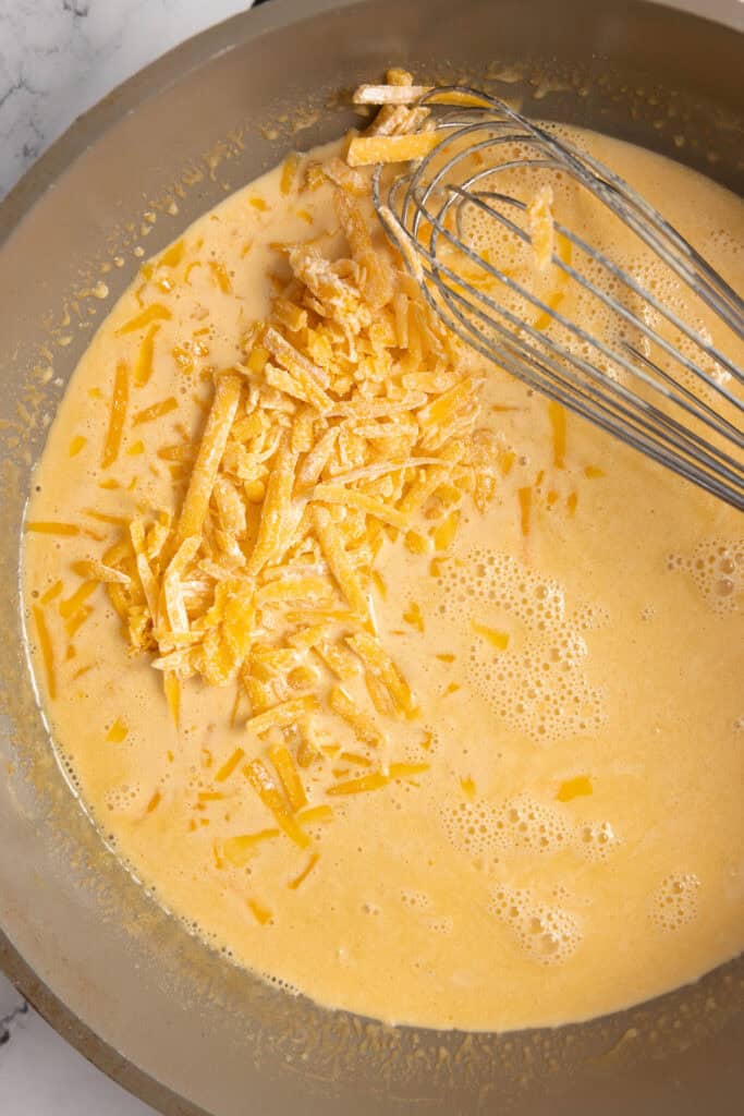 adding sharp cheddar cheese to butter and milk mixture in a saucepan.