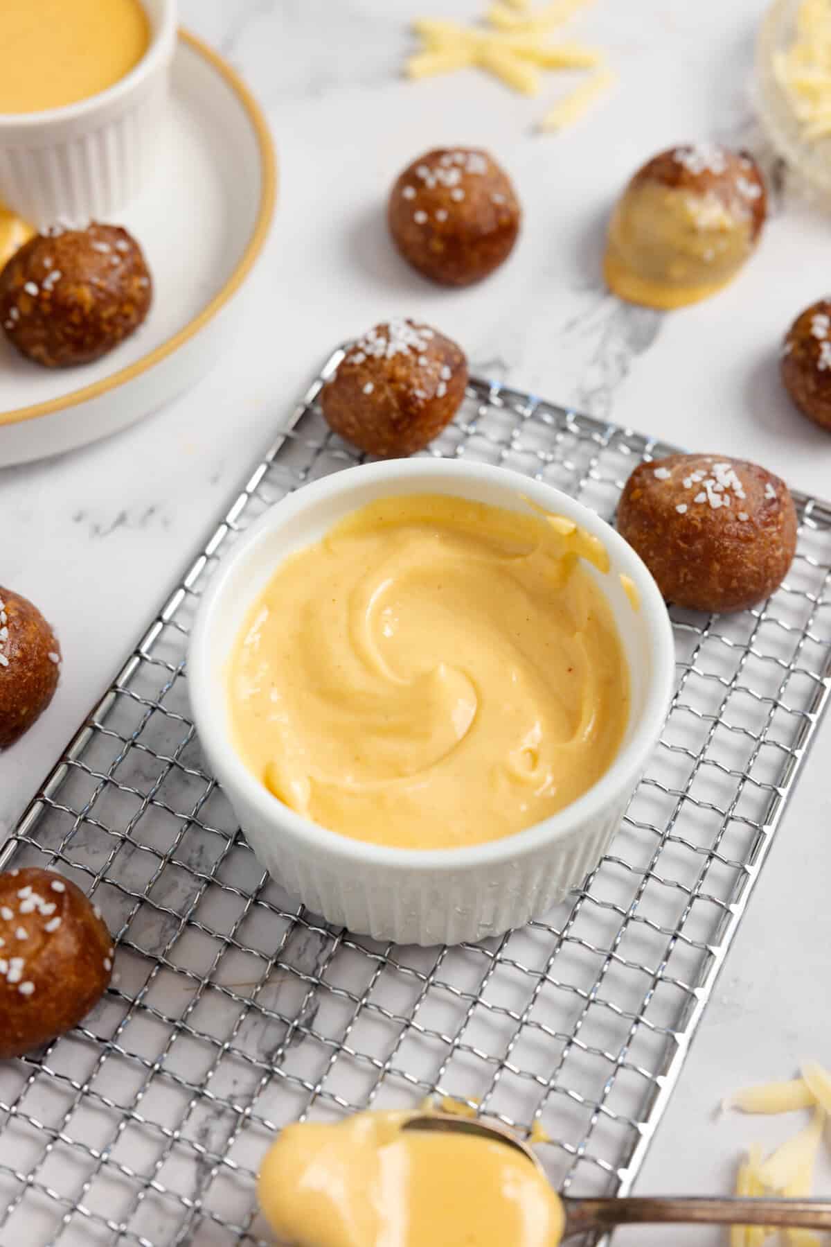 Cheese sauce in a white dish on a white rack surrounded by pretzel bites.