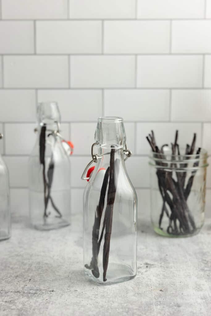 Vanilla beans added to a glass jar with more beans in jars in the background.