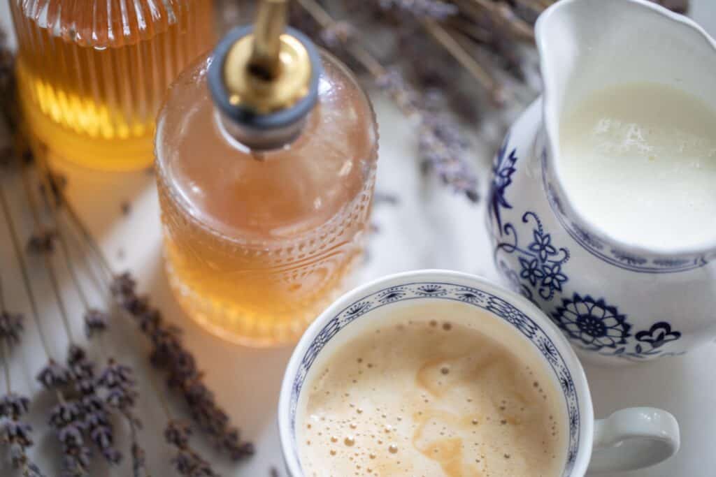 A bottle of lavender syrup next to a latte and cream. 