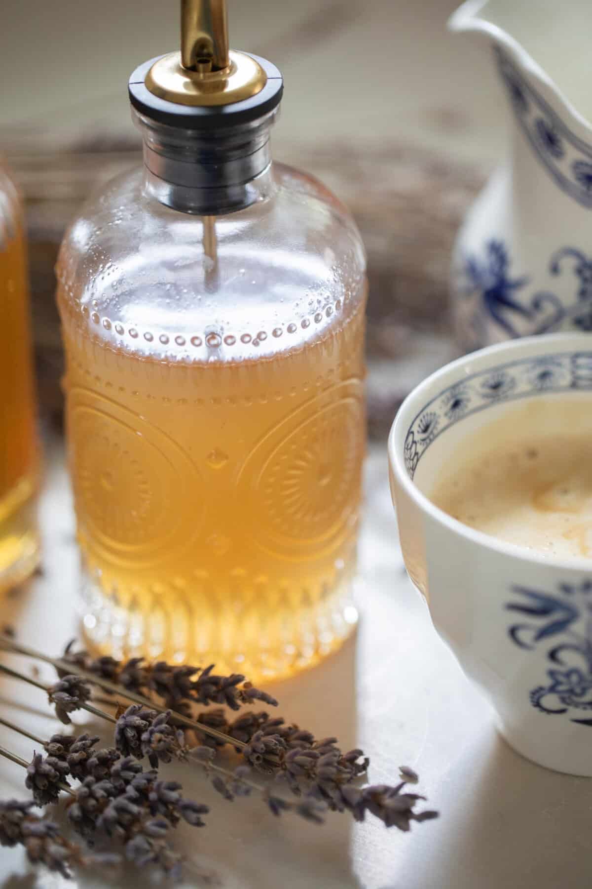 A glass bottle of lavender syrup with fresh lavender on the counter.