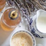 Lavender syrup in a glass bottle next to a homemade latte in a mug.