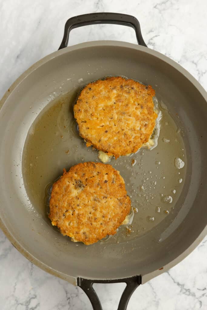 Frying salmon burgers in a skillet.