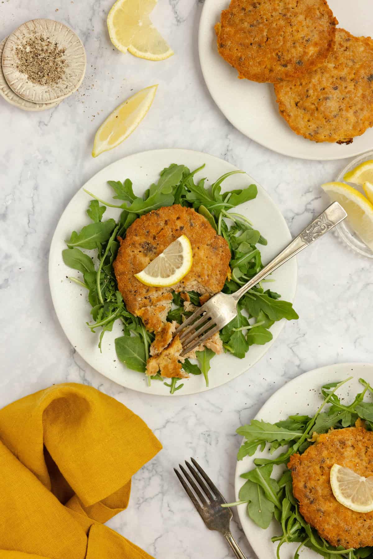 salmon croquettes on a bed of lettuce on a white plate. More salmon burgers  on other plates.