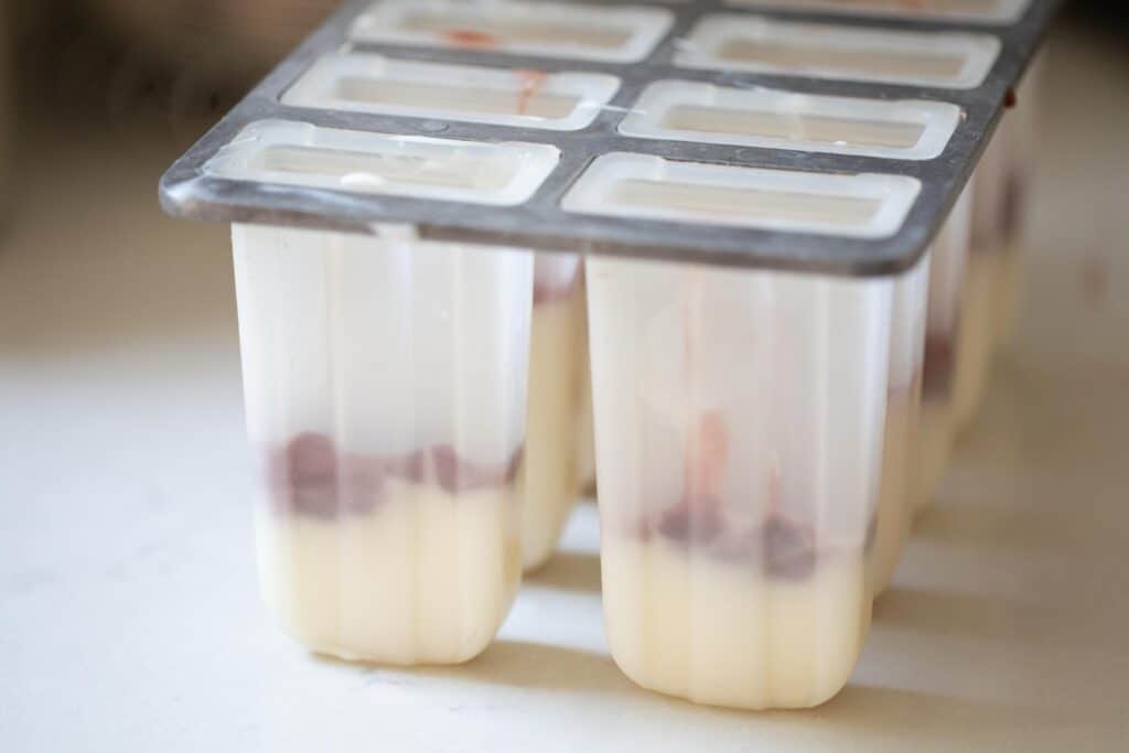 A layer of yogurt and strawberry jam in a popsicle mold.