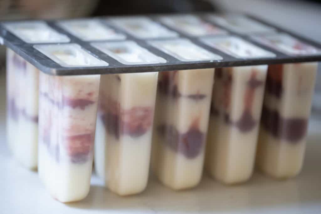 A popsicle mold filled with layers of yogurt and strawberry jam. 