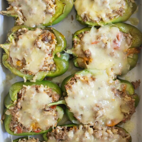 Ground beef stuffed bell peppers with cheese in a white baking dish.