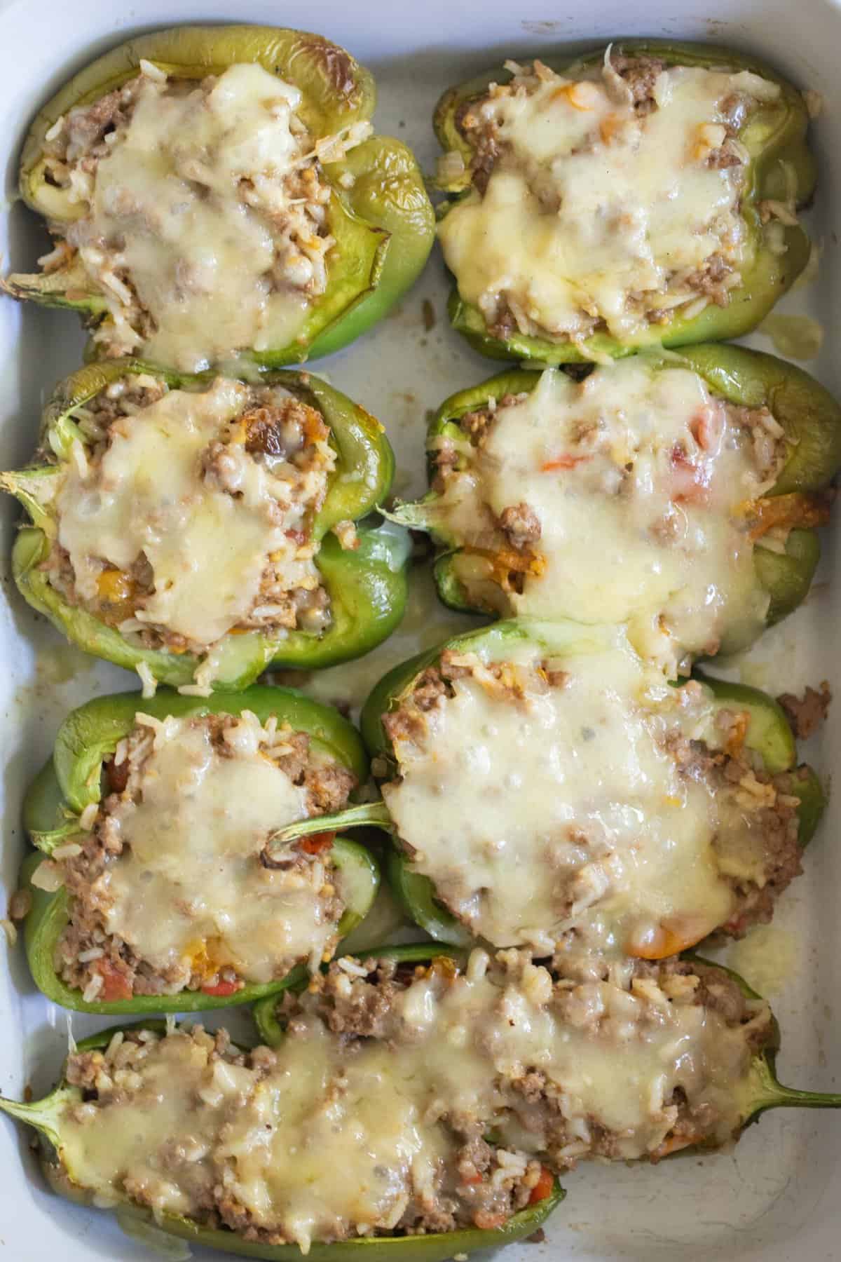 Ground beef stuffed bell peppers with cheese in a white baking dish.