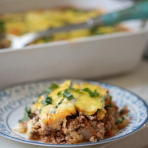 zucchini lasagna on w white plate with a baking dish of more lasagna in the background.