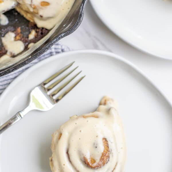 Cinnamon roll topped with icing on a cream colored plate.