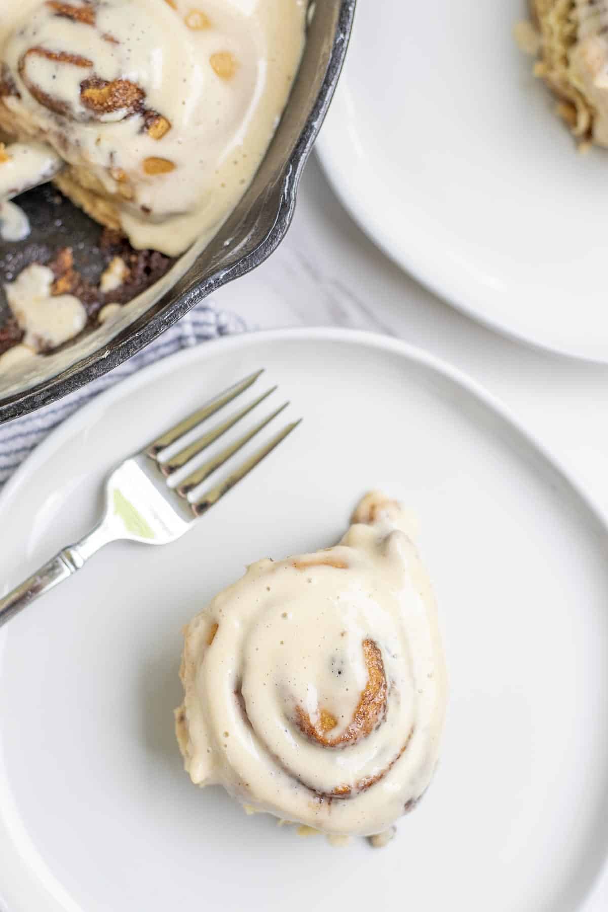 Cinnamon roll topped with icing on a cream colored plate.