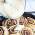 pouring cinnamon roll icing over cinnamon rolls.