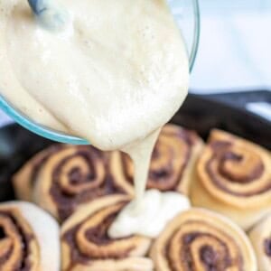 pouring cinnamon roll icing over cinnamon rolls.