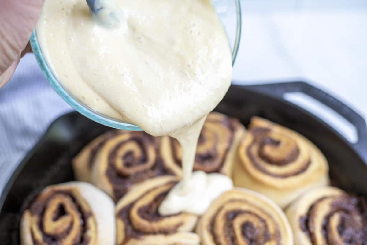 Pouring cinnamon roll icing over cinnamon rolls.