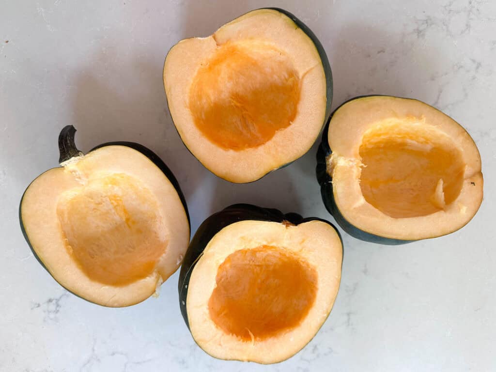 Four acorn squash halves, cut side up on a countertop.