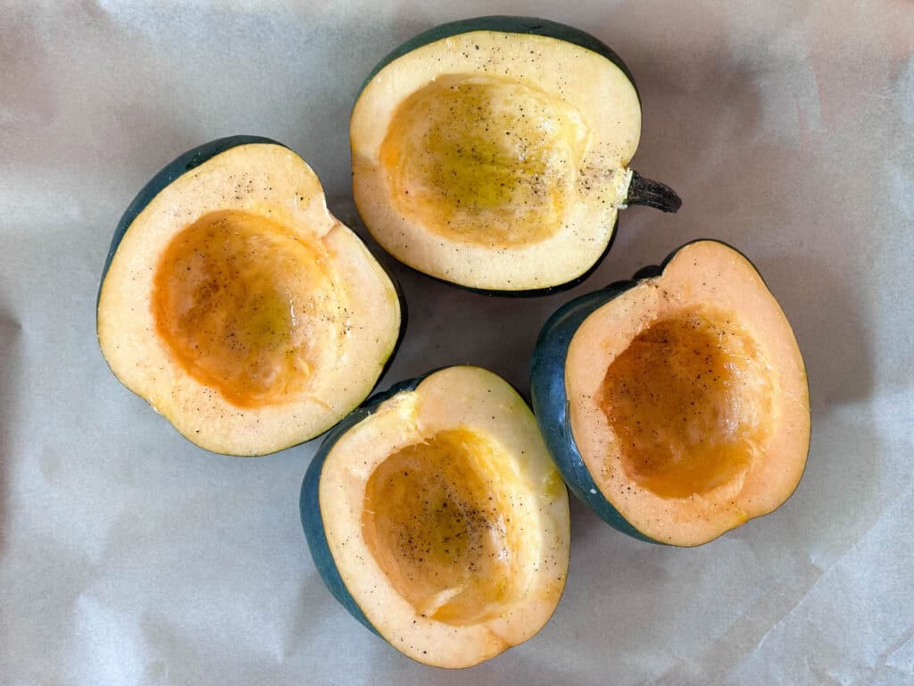 Four halves of acorn squash drizzled with olive oil on parchment paper.