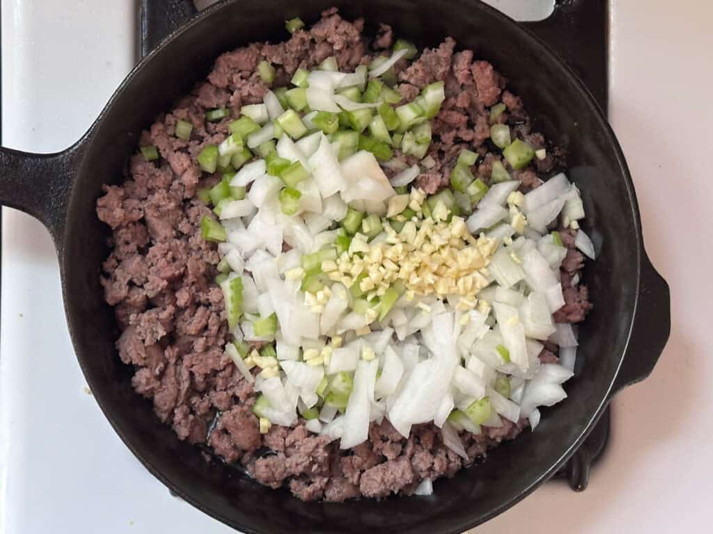 Cooked sausage in a cast iron skillet with onion and other chopped veggies added.