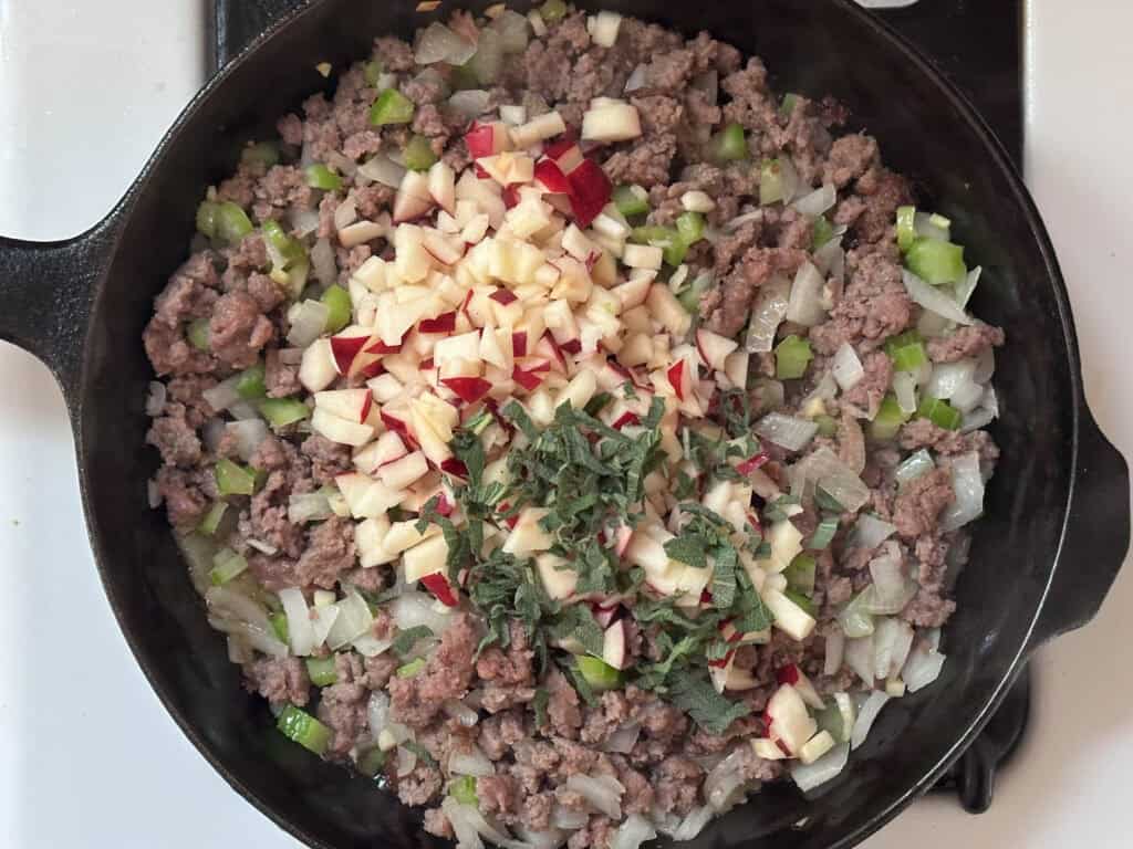 Cooked sausage with added ingredient, such as apples and fresh sage, in a cast iron skillet.