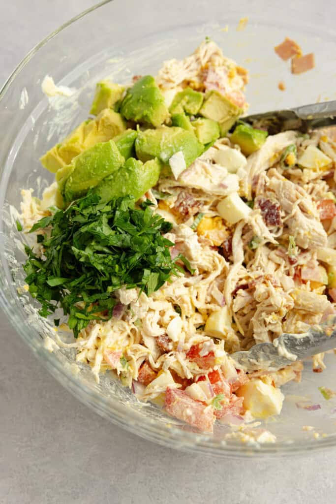 A bowl of chicken salad with avocado chunks and fresh chopped parsley on top.