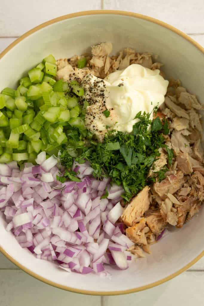 Tuna, onion, celery, fresh herbs, and mayo ready to be mixed together in a bowl.