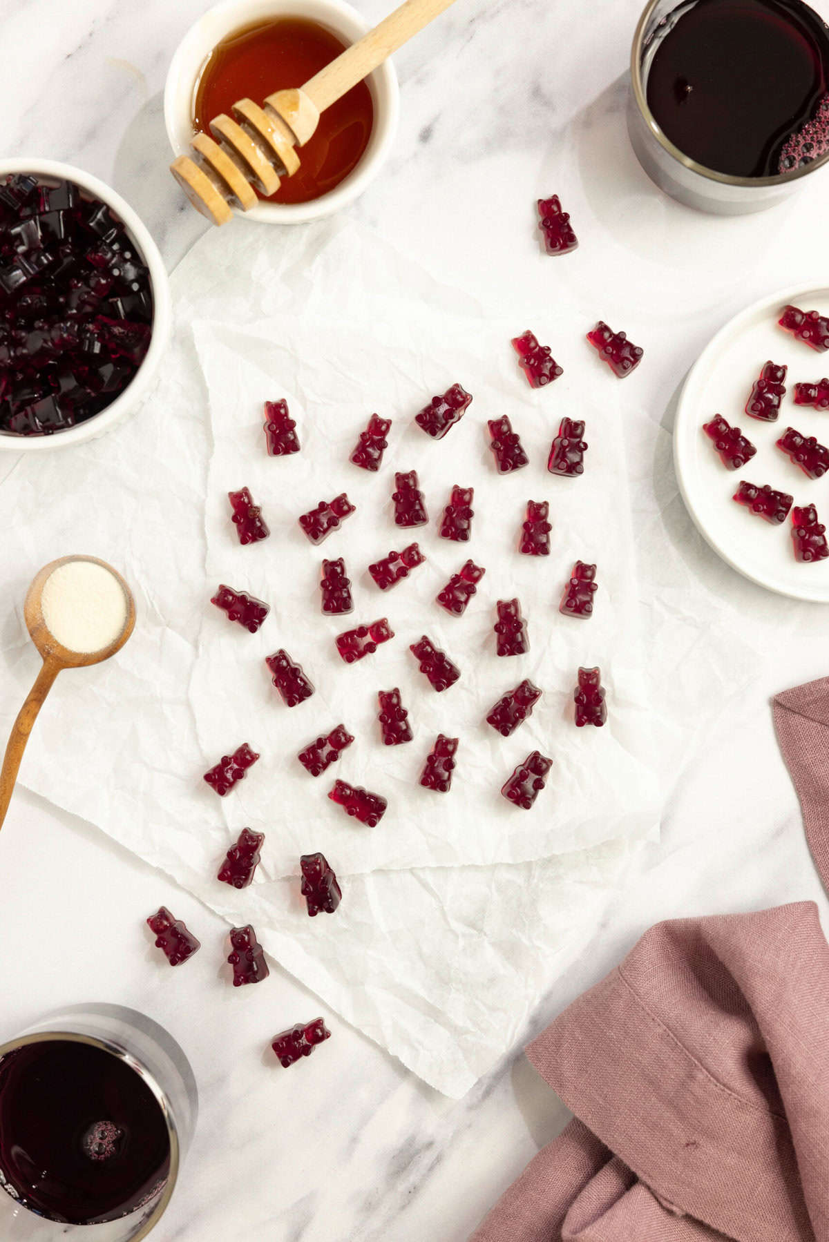 homemade gummy bears scattered on a white countertop with ingredients surrounding the gummy bears.