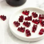 gummy bears on a white plate with a bottle of juice in the background.