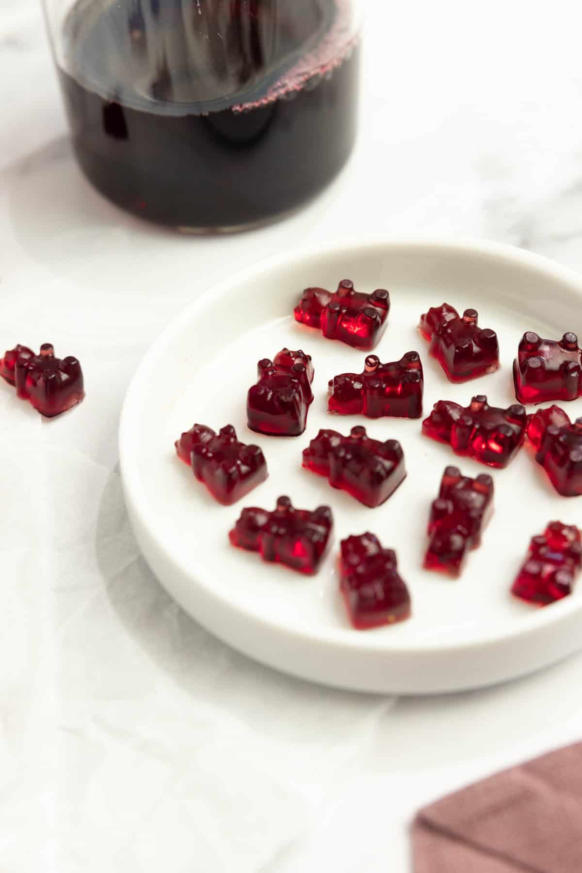 gummy bears on a white plate with a bottle of juice in the background.