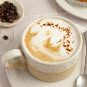 A homemade pumpkin spice latte in a white mug on a white saucer.