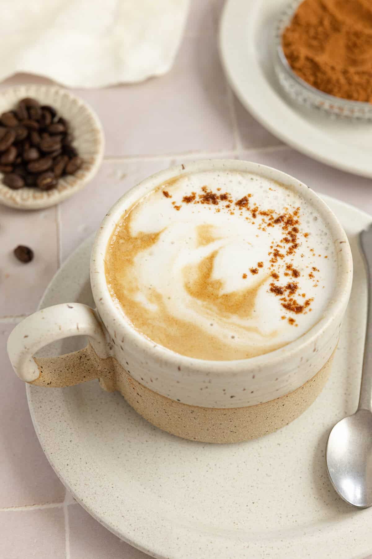 A homemade pumpkin spice latte in a white mug on a white saucer. 