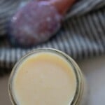 A jar full of sweetened condensed milk with a wooden spoon on the side.