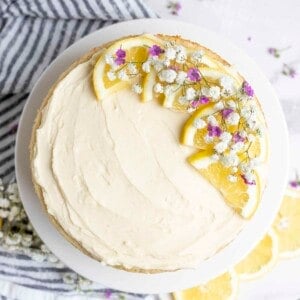 Cake topped with lemon buttercream frosting, sliced lemons and flowers.