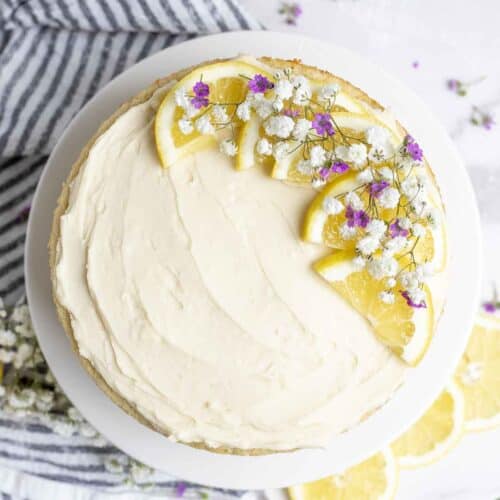 Cake topped with lemon buttercream frosting, sliced lemons and flowers.